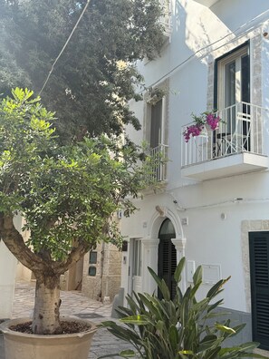 Ein Gebäude mit einem Balkon, einem Topfbaum und einer Steinsäule.