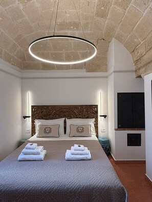 Una camera d'albergo con un letto grande, una testiera in legno, una lampada a soffitto circolare e un televisore appeso al muro.