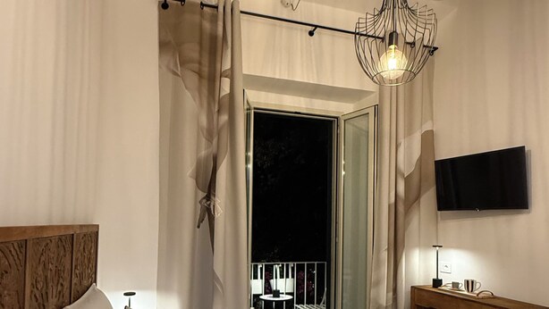 Habitación de hotel con cama, mesita de noche, televisión y vistas a un espacio exterior.