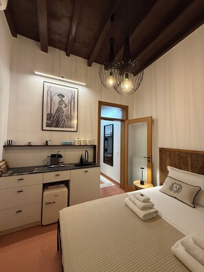 A bedroom with a bed, bedside table, and a nightstand. There is a kitchen area with a sink, cabinets, and a countertop. A framed picture hangs on the wall above the bed. - Angel Apartment 2 - One Bedroom Apartment, Sleeps 2 (Monopoli)