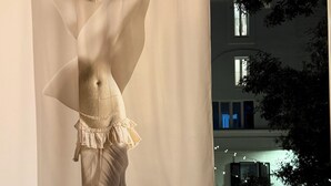 Una habitación con una gran escultura abstracta, un balcón con sillas y vistas a un edificio con ventanas.