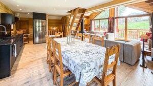 A wooden cabin interior with a dining area, kitchen, and large windows. - Chalet Alpenroc - Valloire (Valloire)