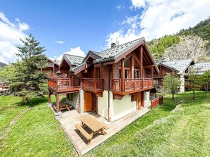 Ein Chalet-Hotel mit mehreren Holzbalkonen, einer Holzterrasse und einem Bergpanorama.
