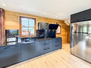 A modern kitchen with wooden walls, a stainless steel refrigerator, and a built-in oven. - Chalet Alpenroc - Valloire (Valloire)