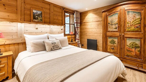 A wooden-paneled bedroom with a bed, nightstands, and a cabinet with artwork. - Chalet Alpenroc - Valloire (Valloire)