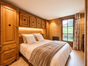Een houten slaapkamer met een bed, nachtkastje en een raam met gordijnen.