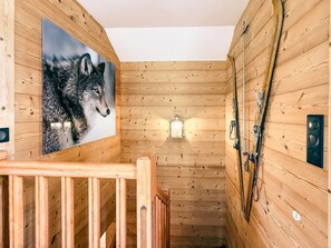Interior de cabana de madeira com escada de madeira, quadro com lobo, lanterna e cabo de teleférico.