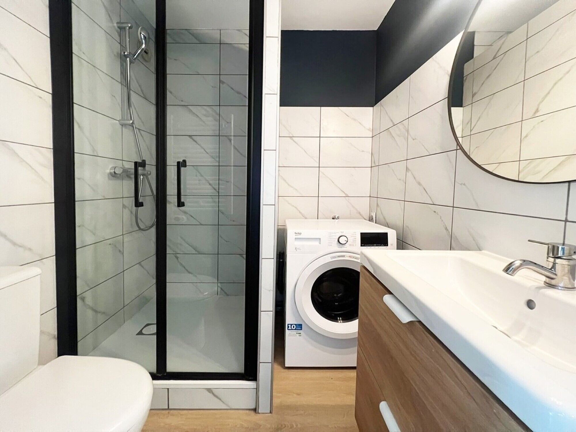 Une salle de bain moderne dotée d’une douche à parois de verre, d’un lave-linge encastré et d’un meuble-lavabo en bois.