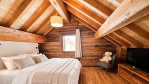 A cozy wooden cabin bedroom with a bed, a chair, a television, and a window. - Chalet Natura Lodge Valloire – Elegant Retreat for 10 Guests with Sauna and Mountain Views (Valloire)