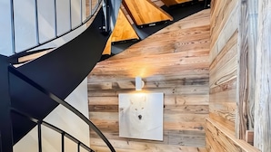 A spiral staircase with wooden steps and black railings, leading to a landing with a wall-mounted light fixture. - Chalet Natura Lodge Valloire – Elegant Retreat for 10 Guests with Sauna and Mountain Views (Valloire)