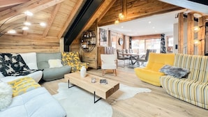 A loft-style room with a high ceiling, wooden beams, a dining area, and a sofa set. - Chalet Natura Lodge Valloire – Elegant Retreat for 10 Guests with Sauna and Mountain Views (Valloire)