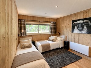 Camera da letto con pareti in legno, due letti, una finestra con tende e un termosifone, con un'opera d'arte a tema pecora.