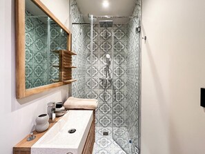 Un bagno con un mobile lavabo in legno, uno specchio grande, una doccia con piastrelle decorate e un porta asciugamani.