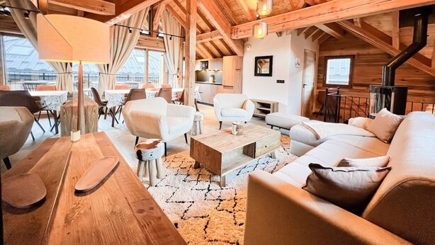 Amplio loft con techos altos, vigas de madera, chimenea y un ventanal grande con vistas a una terraza.