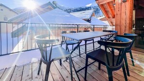 Terraza de madera con una mesa y sillas, con vistas a un paisaje montañoso nevado.
