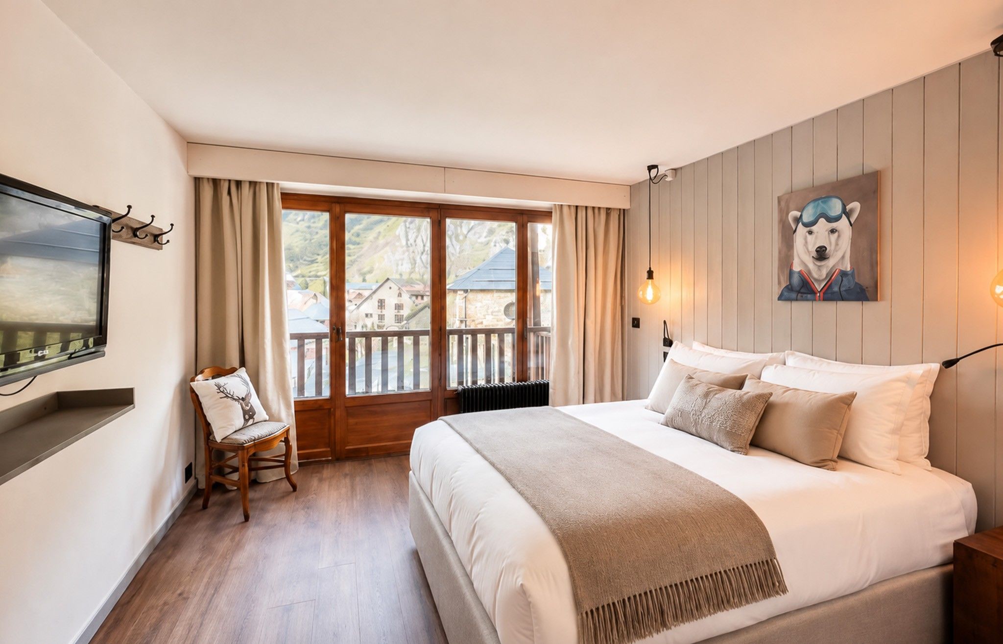 A hotel room with a bed, a chair, a painting, and a window with a view of buildings.