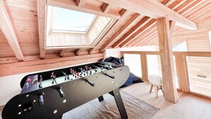 Een kamer met een houten plafond, een tafelvoetbaltafel en grote ramen.