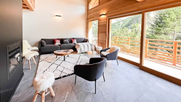 Een ruime kamer met een houten plafond, een zithoek, een salontafel en uitzicht op het omliggende landschap.