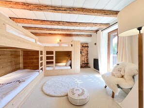 Ein gemütliches Zimmer mit einem Etagenbett, einem runden Teppich, einem kuscheligen Sessel und einem kleinen, runden Tisch mit Kissen.