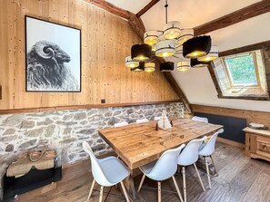 Ein Essbereich mit einem Holztisch, weißen Stühlen, einer Steinwand, einer Illustration eines Schafs und einer Kristallleuchter.