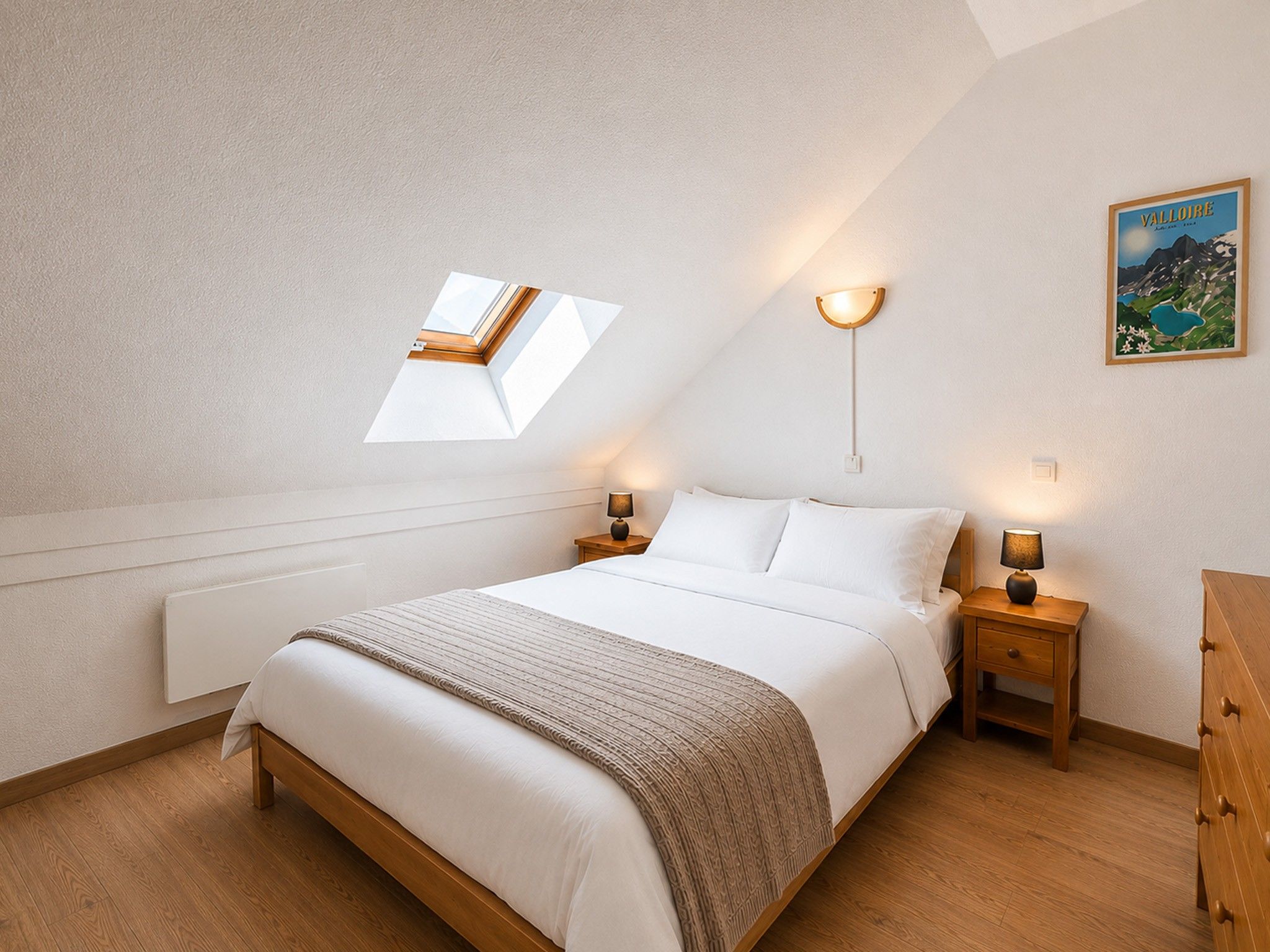 A bedroom with a skylight, a bed with white linens, two bedside lamps, and a framed picture on the wall.