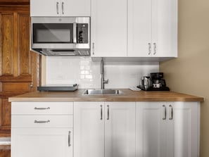 A kitchen with white cabinets, a stainless steel sink, a microwave, and a coffee maker.