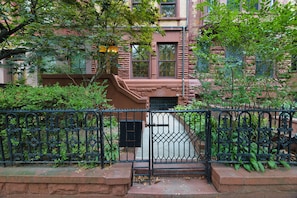 A brick building with a gated entrance, surrounded by greenery and a metal fence. - Hamilton House Apt 6 with Pvt Bathroom (New York)