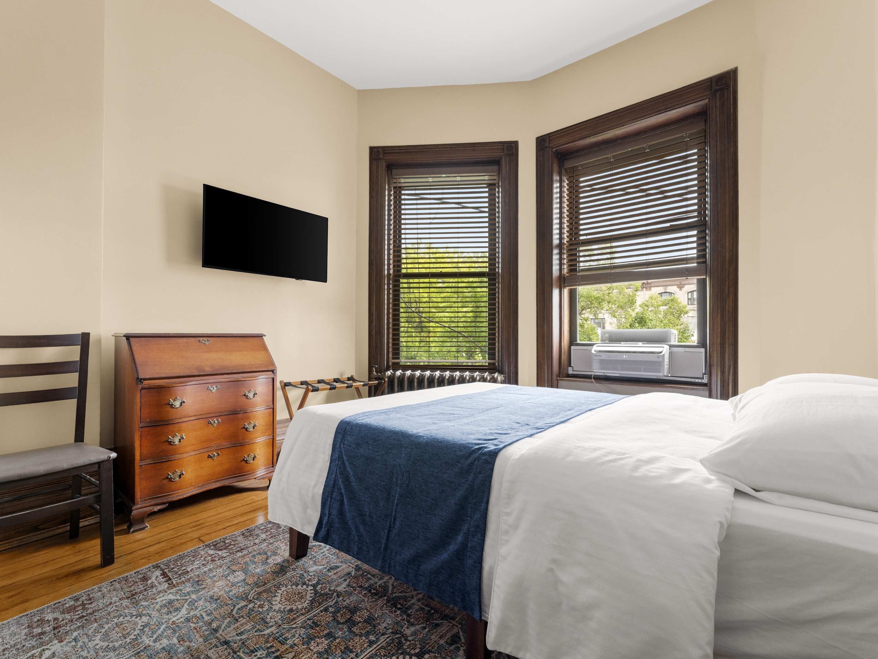 A bedroom with a bed, dresser, chair, and a TV mounted on the wall.