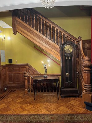 A grand staircase with a wooden handrail and balusters, a large wall-mounted clock, and a table with a statue.