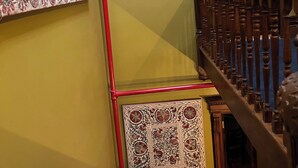 A staircase with a wooden handrail, a red pipe running vertically, and a framed abstract painting on the wall.