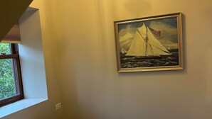 A bedroom with a bed, a window, a painting of a sailboat, and a chandelier.
