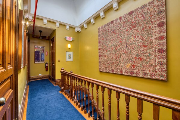 A hallway with a blue carpet, wooden railing, and a large floral artwork on the wall.