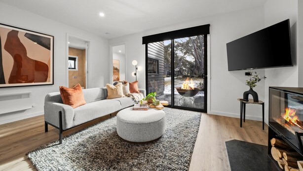 A modern living room with a grey sofa, round ottoman, and a flat-screen TV. - Dinner Plain Mt Hotham Accommodation (Dinner Plain)