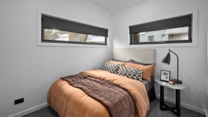A bedroom with a bed, two windows with blinds, a bedside table with a lamp, and a framed picture. - Dinner Plain Mt Hotham Accommodation (Dinner Plain)