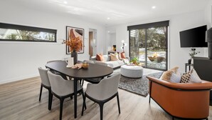 A modern living room with a dining area, large windows, and a flat-screen TV. - Dinner Plain Mt Hotham Accommodation (Dinner Plain)