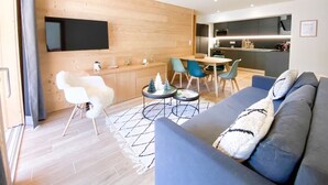Een moderne woonkamer met een bank, een eethoek met stoelen, een keuken en een wandgemonteerde televisie.
