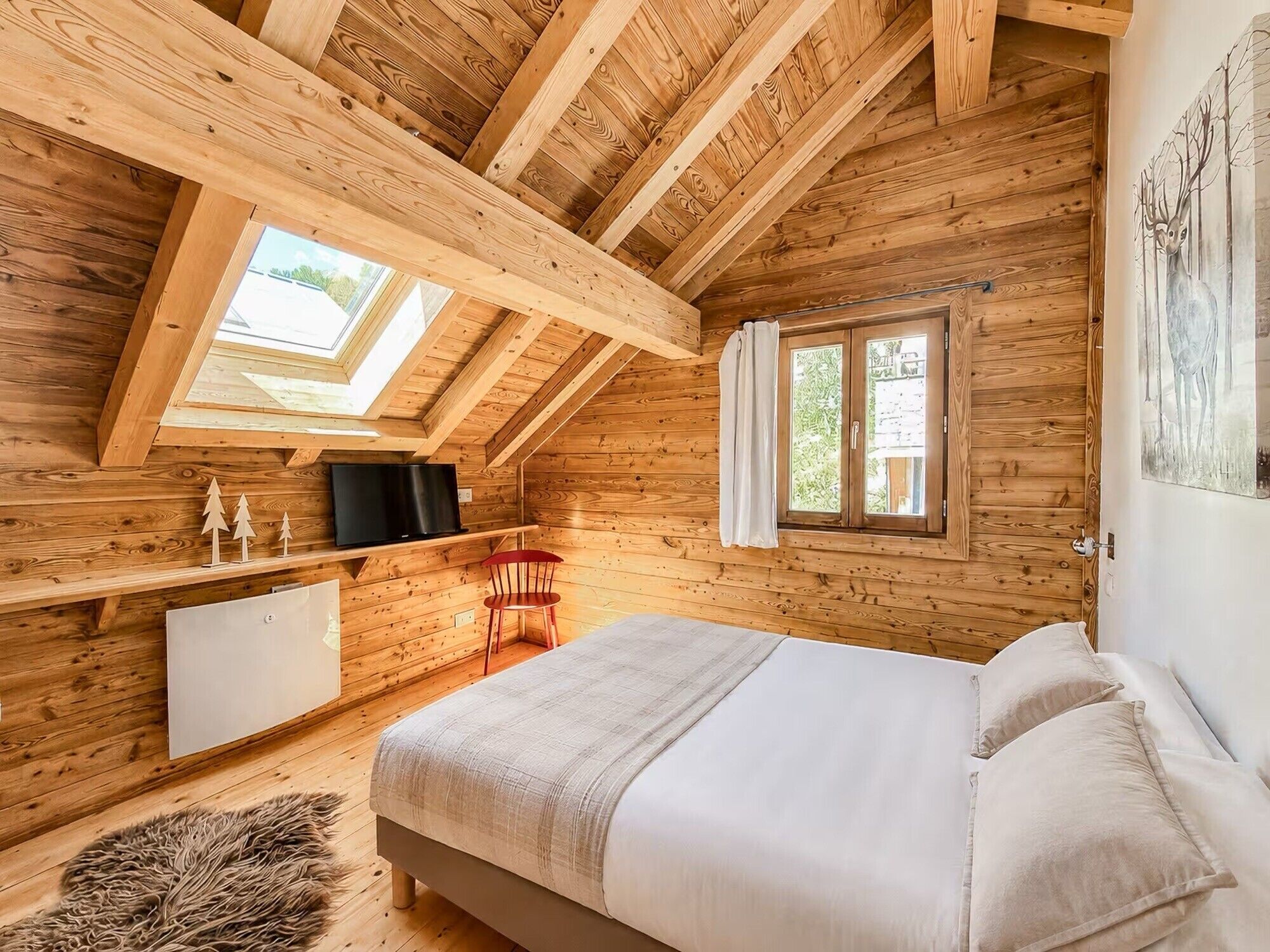 A cozy wooden cabin bedroom with a loft-style ceiling, a bed, a TV, and a window with curtains.
