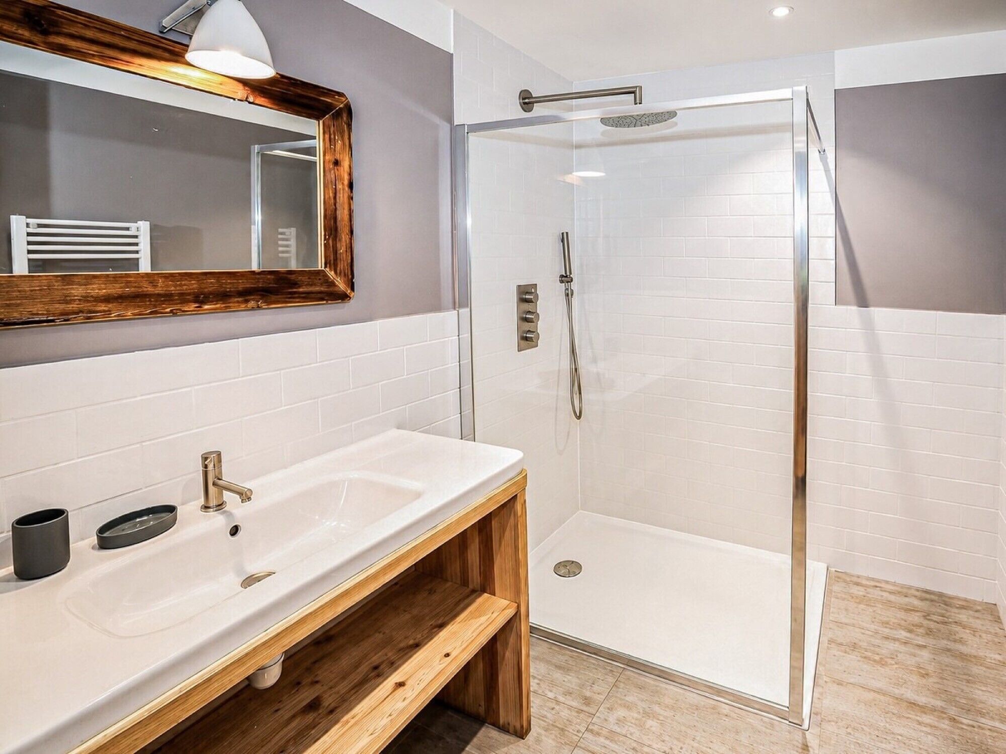 A modern bathroom with a white sink, wooden vanity, a glass shower enclosure, and a mirror with a wooden frame.