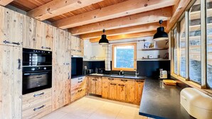 Une cuisine moderne avec des meubles en bois, un îlot central, des appareils électroménagers noirs et un éclairage suspendu.