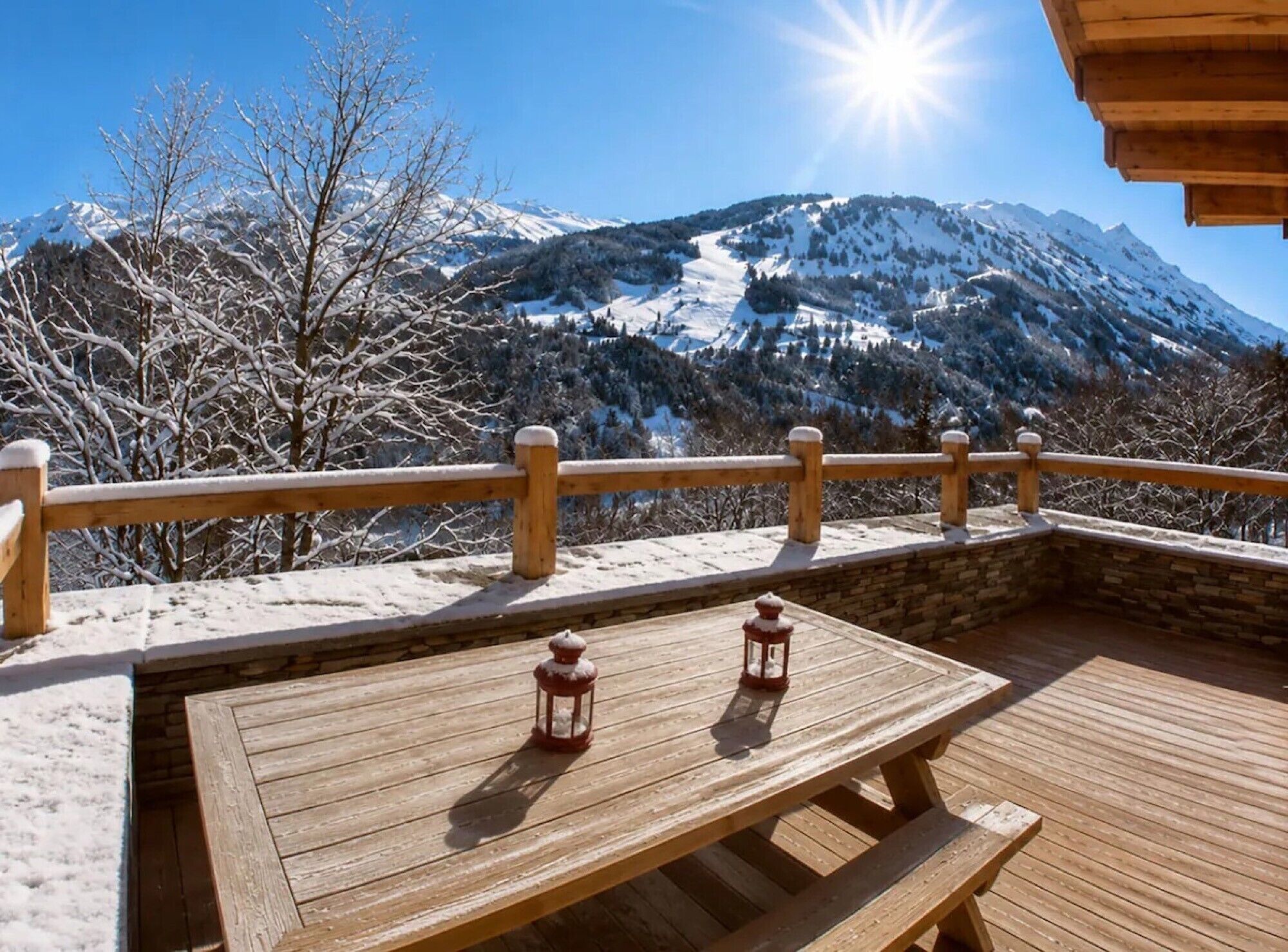 A wooden deck with two lanterns, overlooking a snowy mountain landscape.