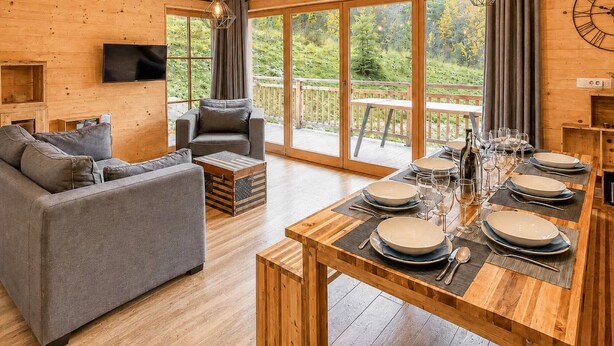 Un interior de madera con un sofá, una mesa de comedor y un televisor montado en la pared.