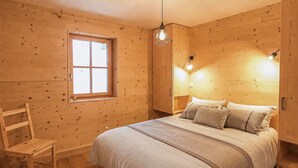 Una habitación de madera con una cama, una ventana, una silla y una lámpara colgante.
