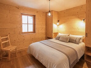 Ein Zimmer aus Holz mit einem Bett, einem Fenster, einem Sessel und einer Pendelleuchte.