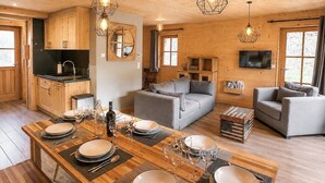 Un interior de madera con una mesa de comedor preparada para seis personas, un sofá, un televisor y armarios de madera.