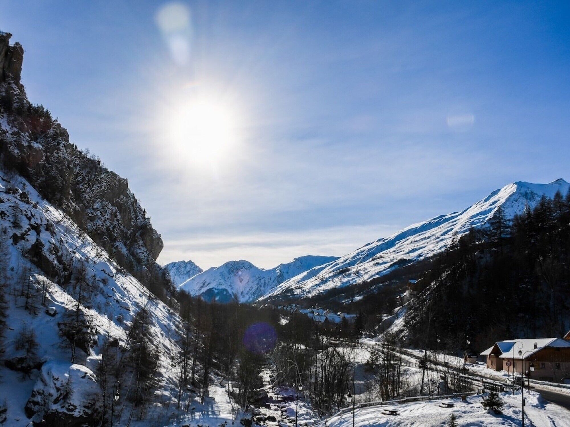 A snow-covered mountain landscape with a clear sky and a sun shining.