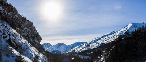 A snow-covered mountain landscape with a clear sky and a sun shining.