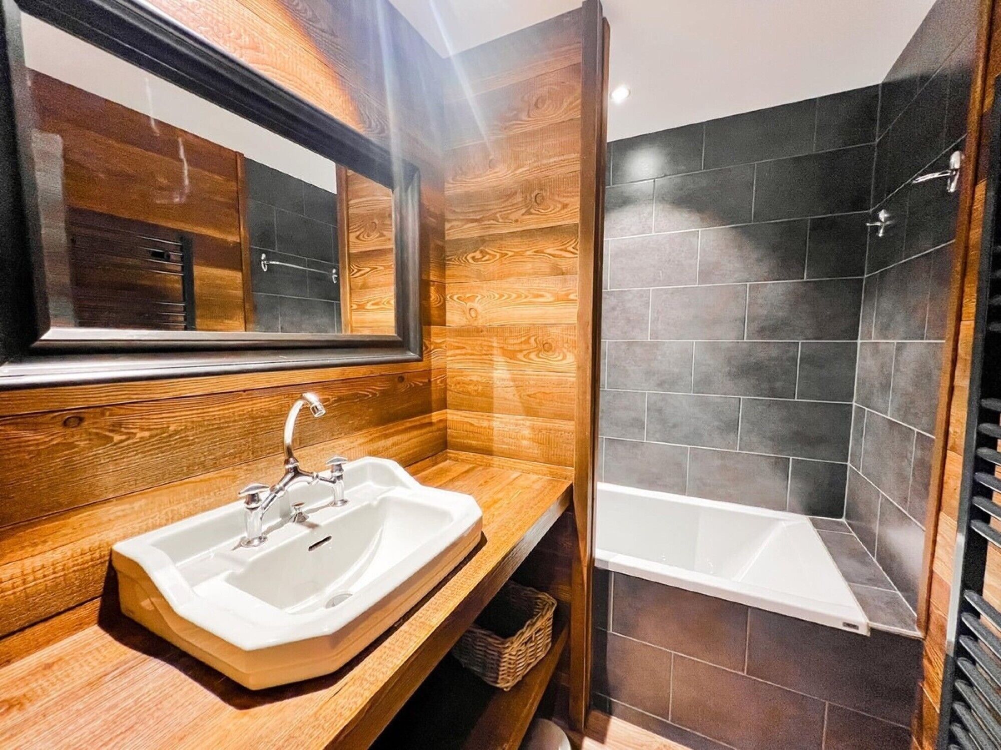 Un baño con tocador de madera, un lavamanos, un espejo y zona de ducha.