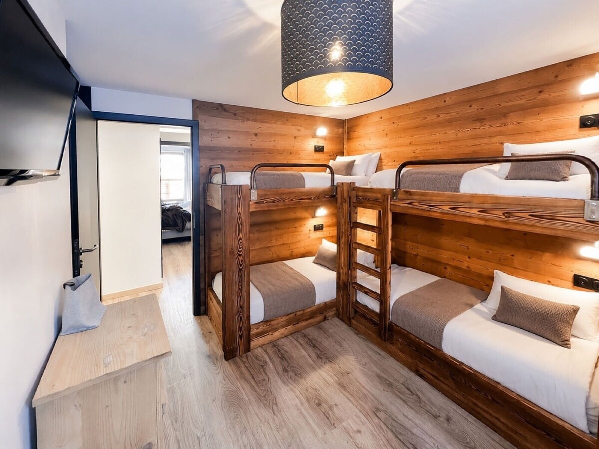 A bunk bed room with wooden walls, a hanging light fixture, and a door leading to another room.