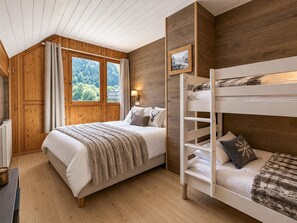 Un dormitorio con una cama, una litera, paredes de madera, una ventana con vistas y un cuadro en la pared.
