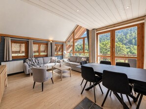 A spacious living area with a high ceiling, large windows, and a view of a forested landscape. - L'Après-Ski Apartment Valloire – Mountain Duplex with Wellness Access (Valloire)